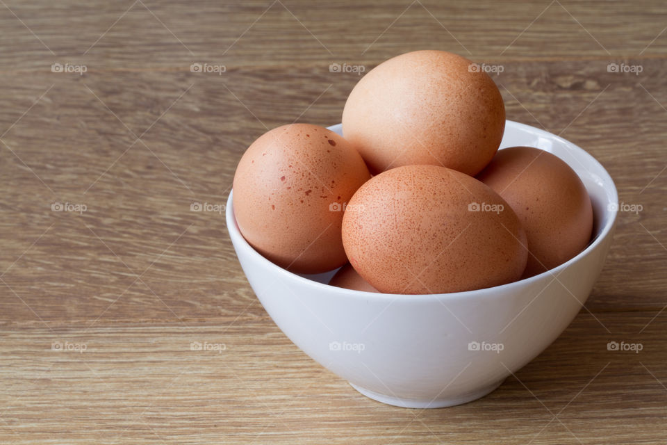 A white bowl full of fresh, brown speckled hen eggs on a wooden table. Simple food shot of eggs.