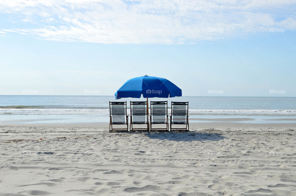 Row of empty lounge chairs and an umbrella on the ocean shore