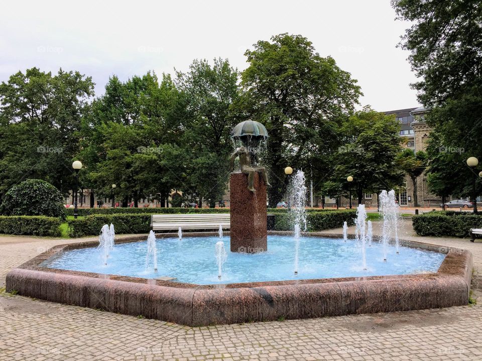 City public park fountain with the figurine of the sitting child under the umbrella 