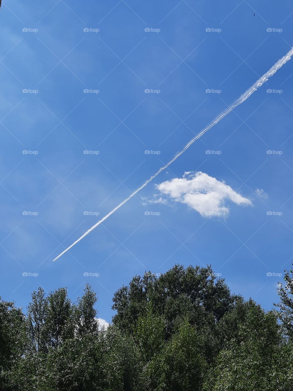 white clouds and condensation stream against blue sky