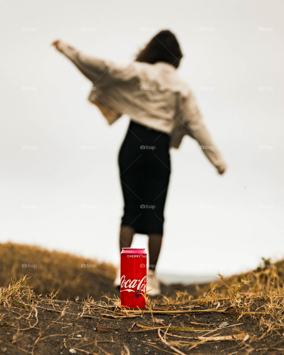 Female walking away from coca cola can on the beach.