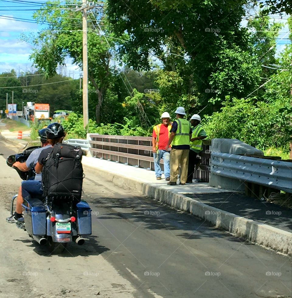 Motorcycle with riders driving past State Architects overlooking bridge and waterway under street. Sunny day and warm weather day.