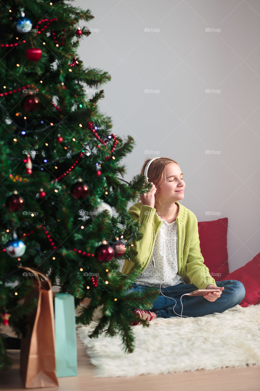 Teenage girl listening music in front christmas tree