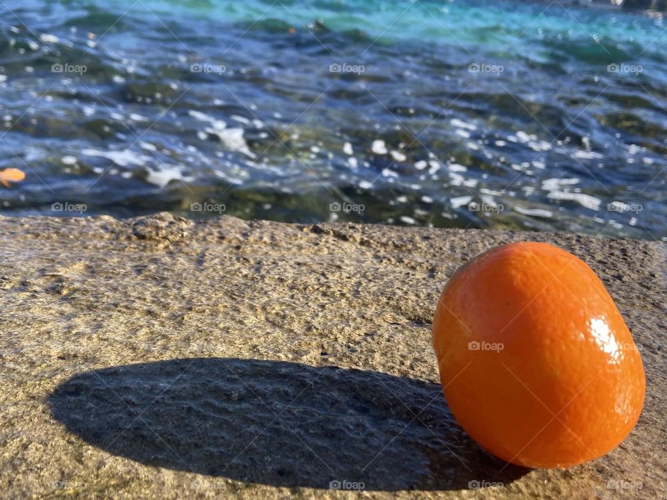 An orange mandarin is left discarded by the blue sea.