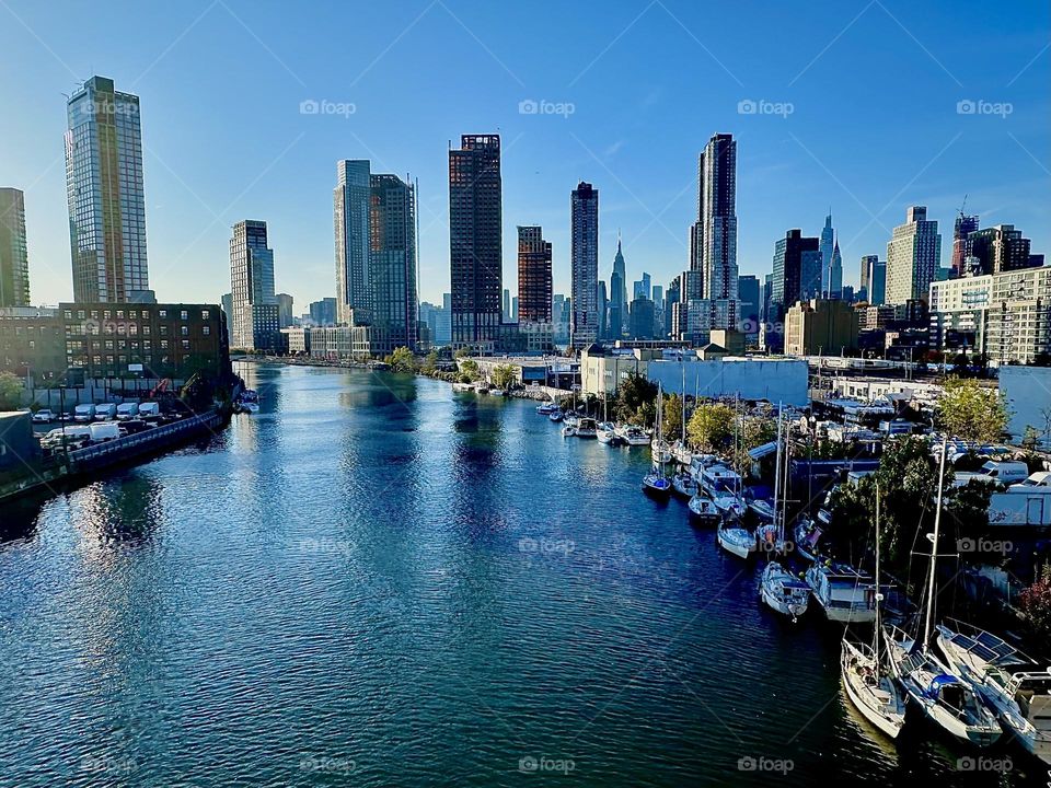 This is beautiful “Newtown Creek” seen from the “Pulaski Bridge” that connects “Greenpoint”, Brooklyn with LIC, Queens. In the distance “Manhattan” including the “Empire State Building” can be seen. 2023. Hypnotic Productions