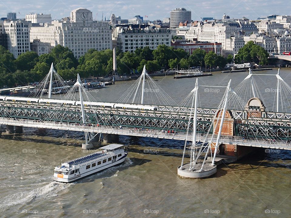 A passenger touring boat floats under a bridge on the Thames River in London, England on a summer day. 