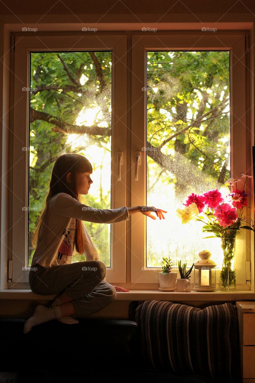 Little girl plays with flowers on a windowsill
