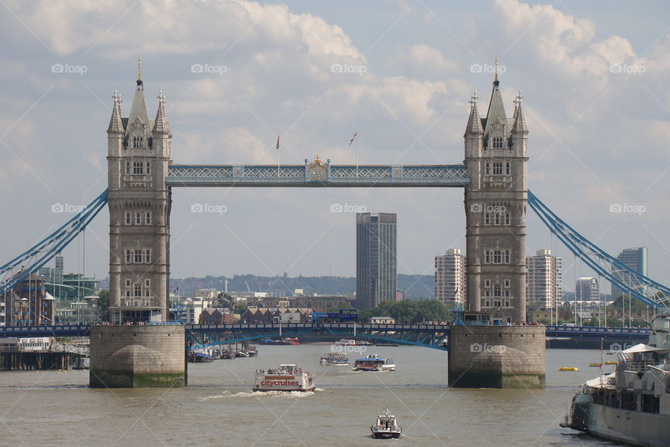 London tower bridge with ships and boats traveling down the river Thames in front of the bridge on a bright blue summer's day.