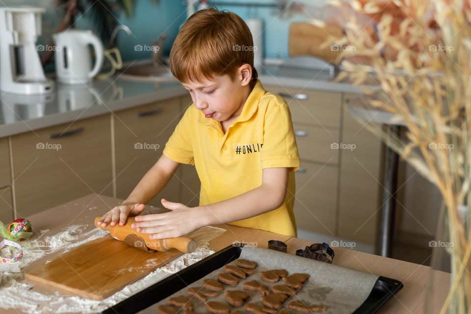 child red-haired boy in a yellow T-shirt bakes homemade muffins cookies at home in the kitchen