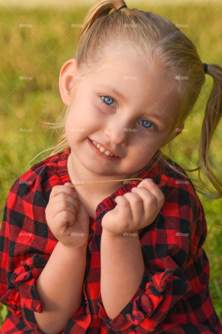 adorable small girl wearing a black and red checkered shirt with pigtails, beautiful bright blue eyes and a great smile