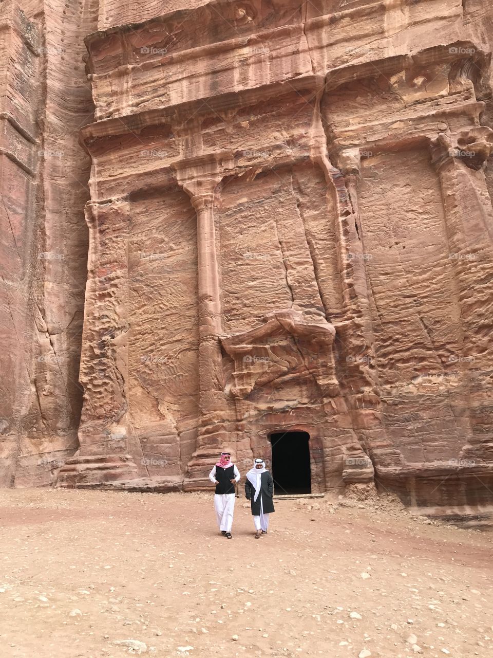 Two Jordanian men walking out of an ancient ruin in Petra, Jordan