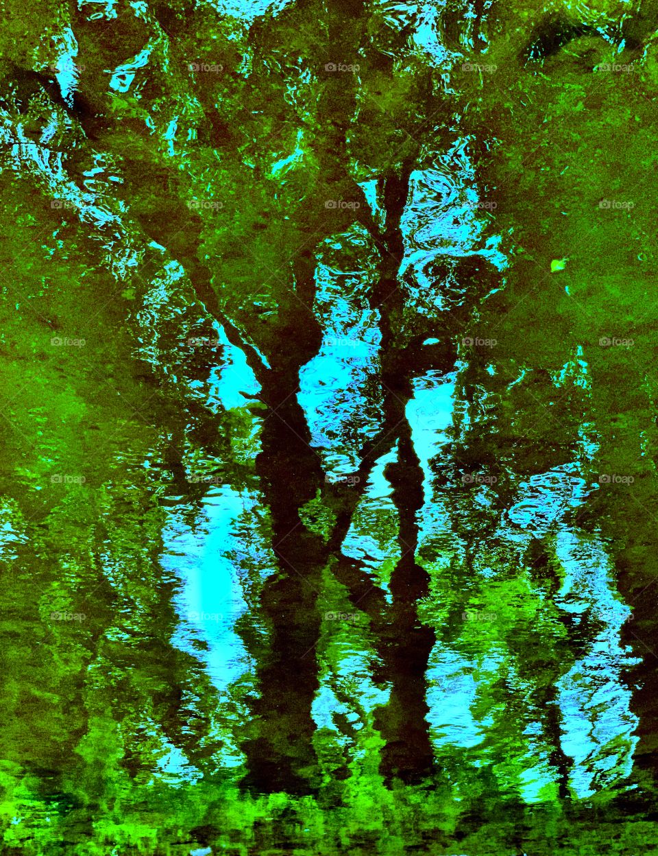 abstract reflection of green leafed trees against blue sky in a rippling pond on a sunny summer’s day