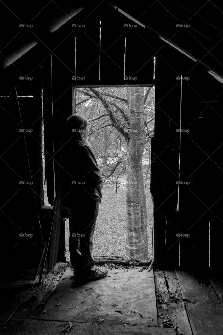 A young girl gazes out of the loft door of an old barn. 