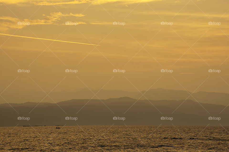 Golden light of sunrise behind the mountains in the sea and shadow fishing boats.