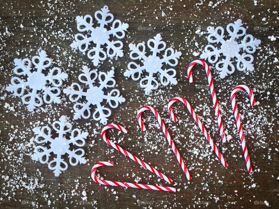Candy canes on rustic wooden table powdered with snow and snowflakes 