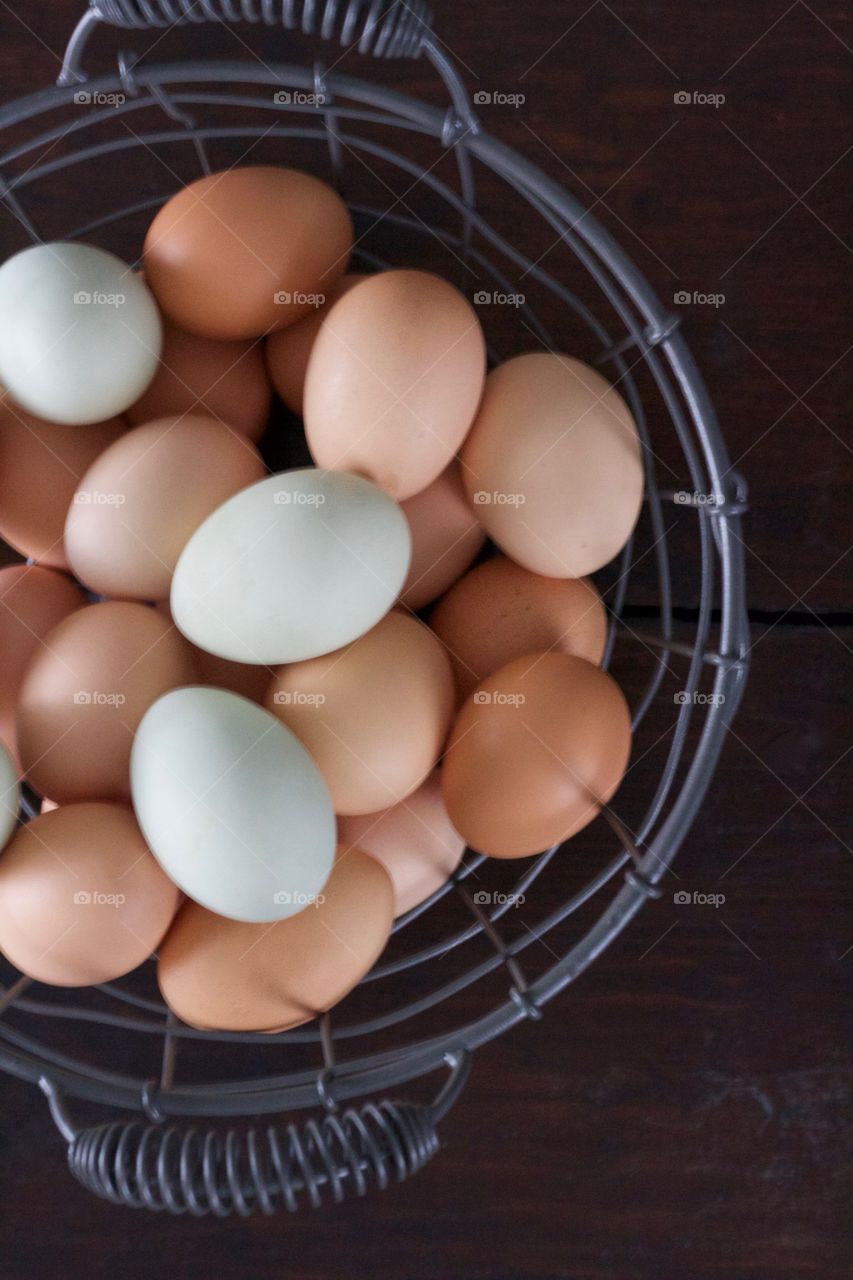 Overhead view of farm-fresh blue and brown eggs in a wire basket on a dark wooden surface