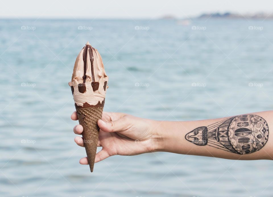 A hand holds an ice cream, sea background