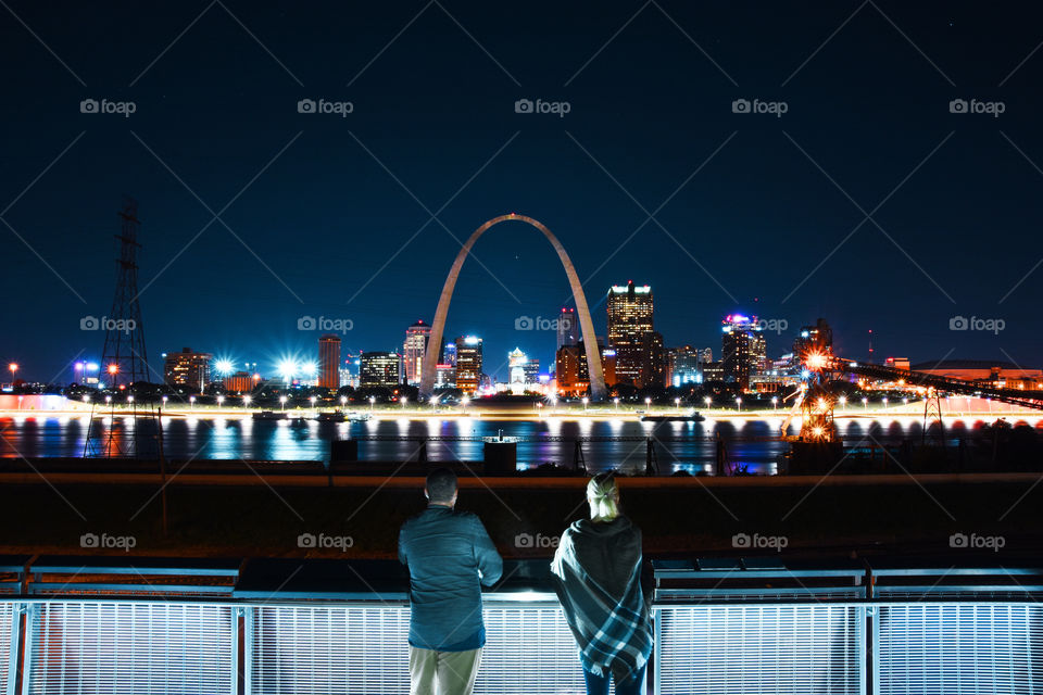 Couple of young adults standing at viewpoint and looking to Gateway arch in St. Louis city in Missouri state , USA at night