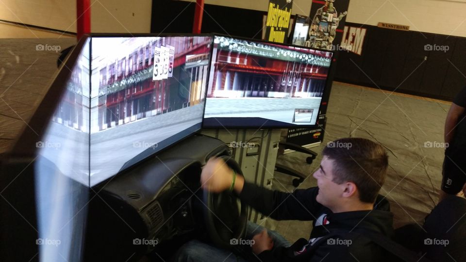 High school teenager participates and practices a distracted driving simulator during an impaired driving seminar in the gymnasium.