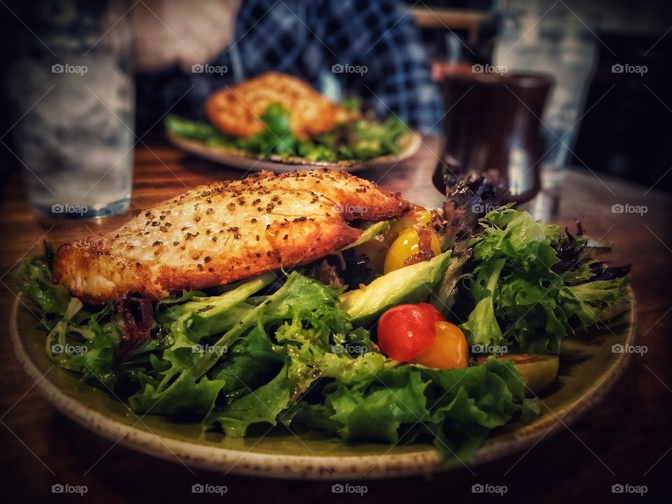 Salmon on a leafy greens salad with tomatoes and avocado