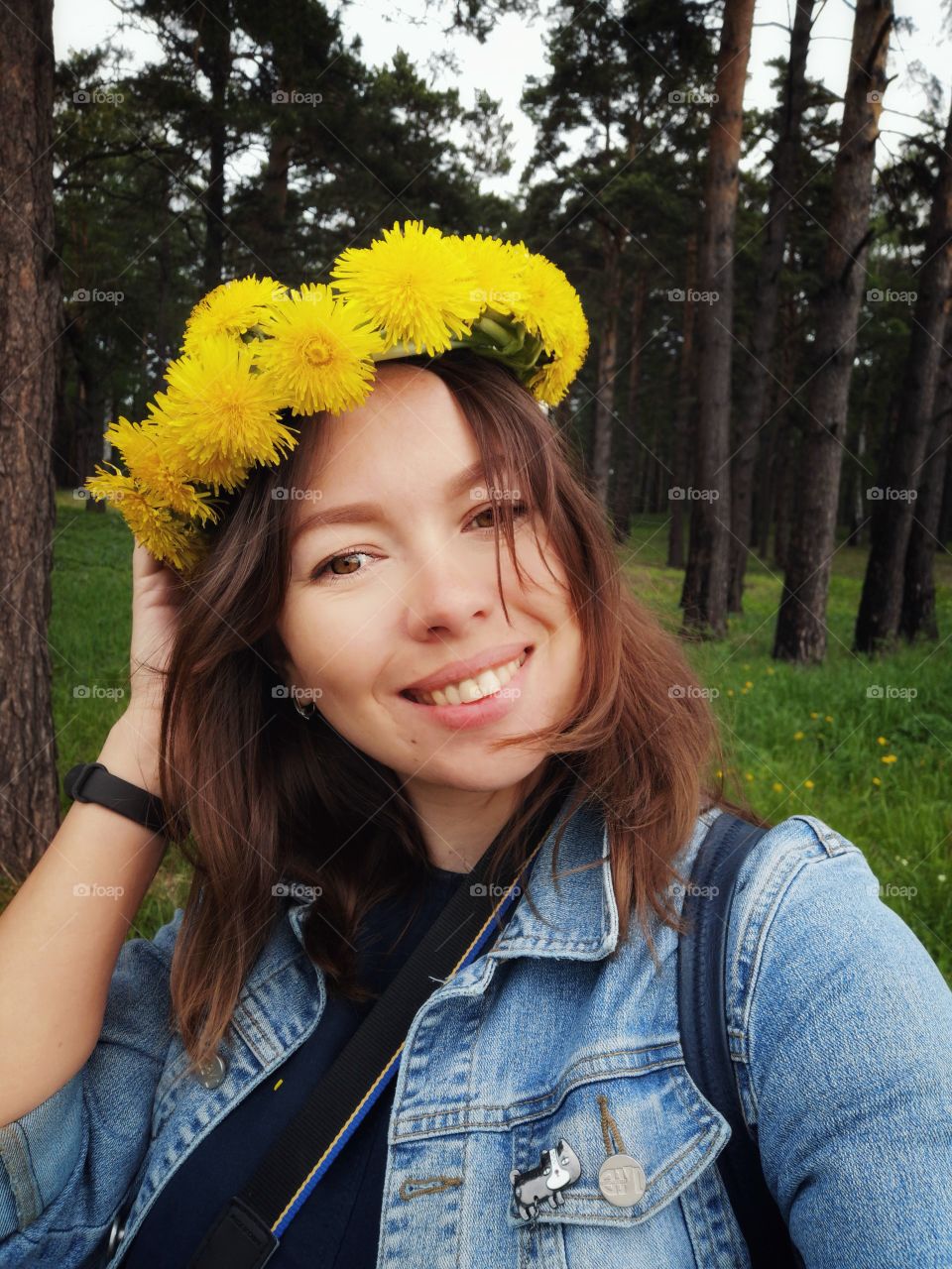 A beautiful girl smiles. She's got a dandelion wreath on her head
