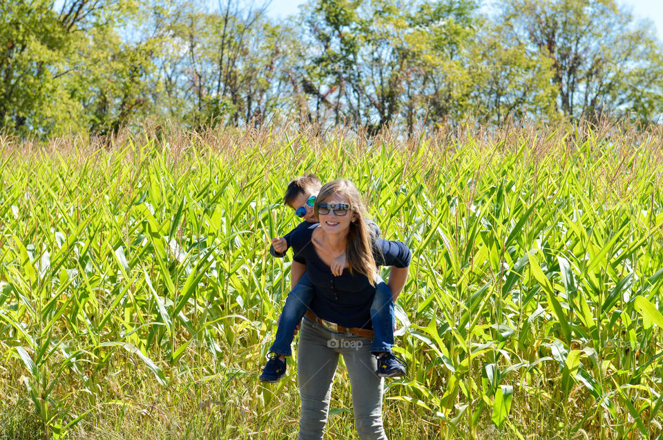 Woman happily holding son on her back in a cornfield