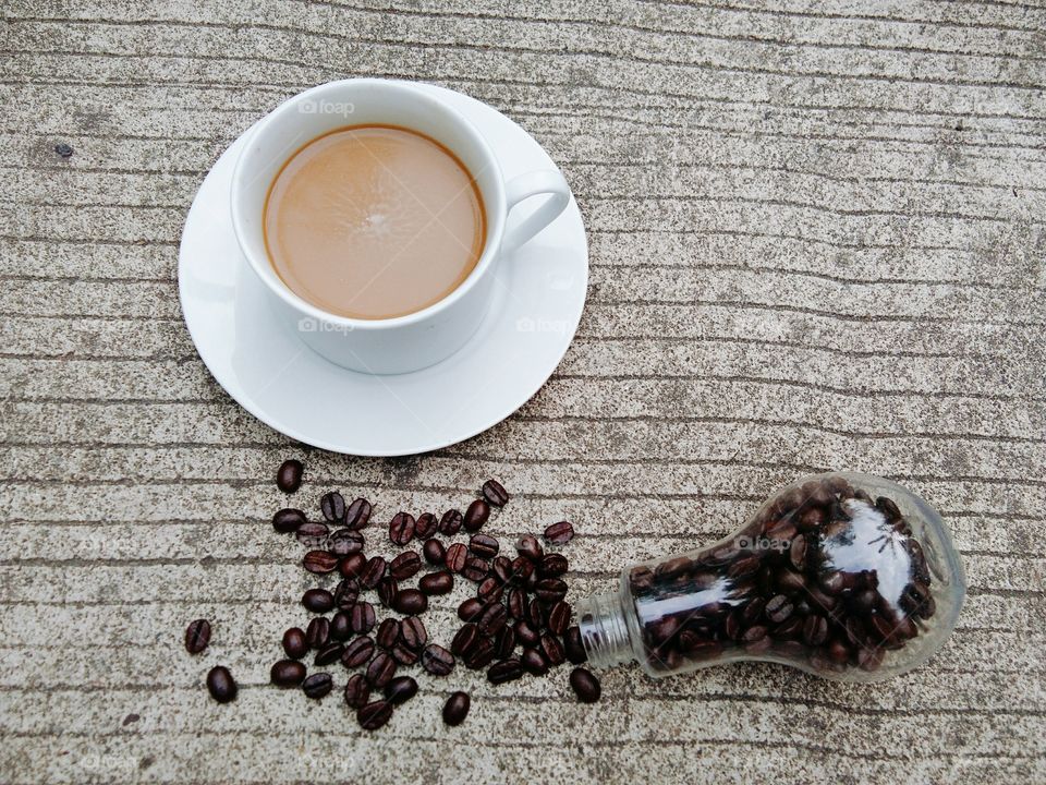 A White cup of coffee and coffee beans in glass bottle on concrete floor