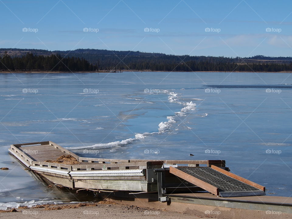 A small boat ramp and dock extends into a frozen over Thompson Reservoir in Southern Oregon on a clear winter day. 