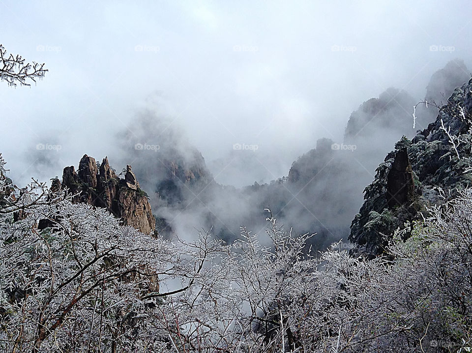 Close by are icy pine trees. On the cliff on the left, there is a huge boulder like a "fairy" with his back facing us. He sits quietly on the top of the cliff and looks at the beautiful scenery of the clouds and mountains in front of him.