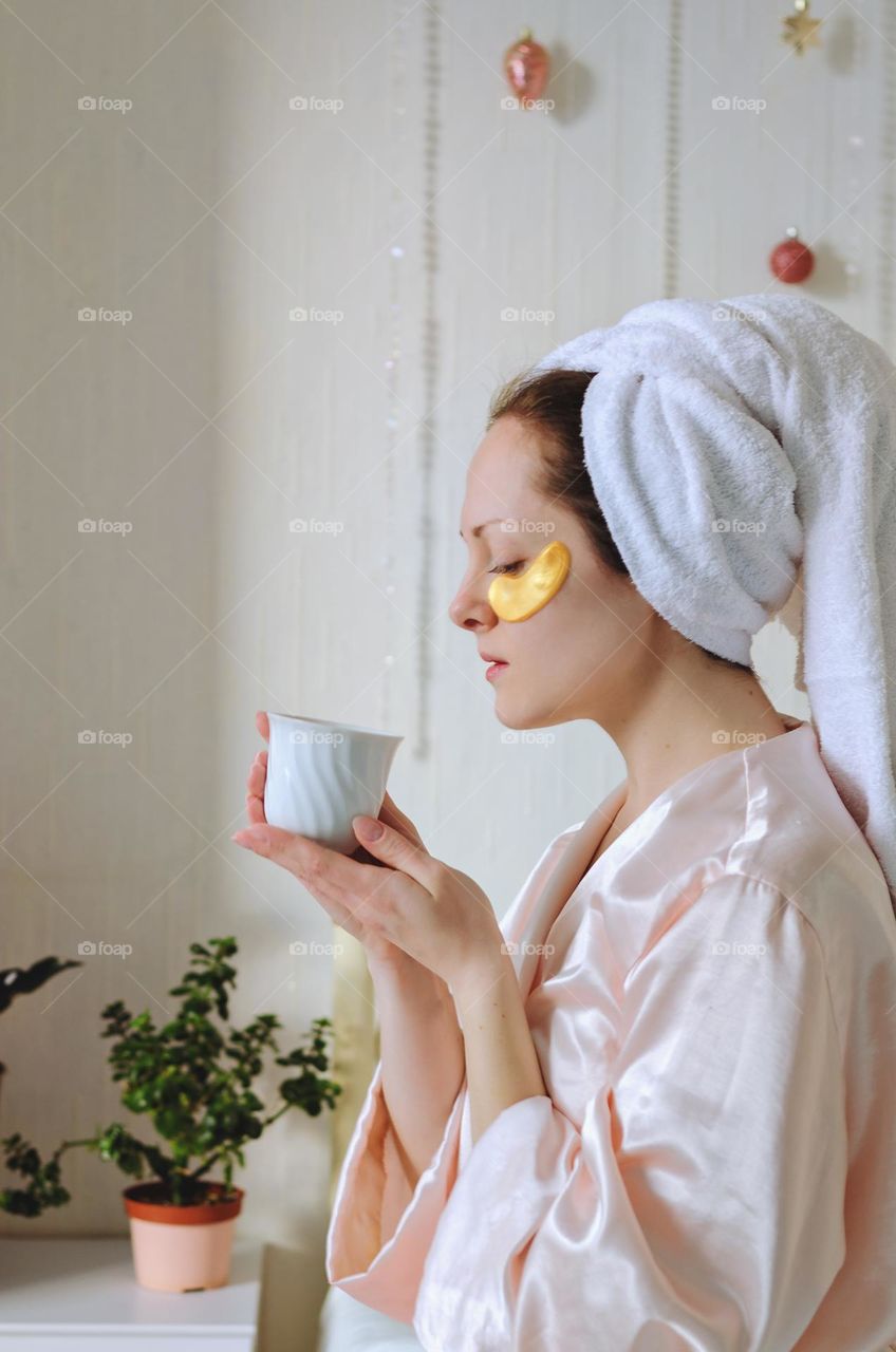 Young happy woman with a towel on head doing facial skin care procedures.   Beauty routine.  Cosmetic concept.  Patches at the face. Wellness