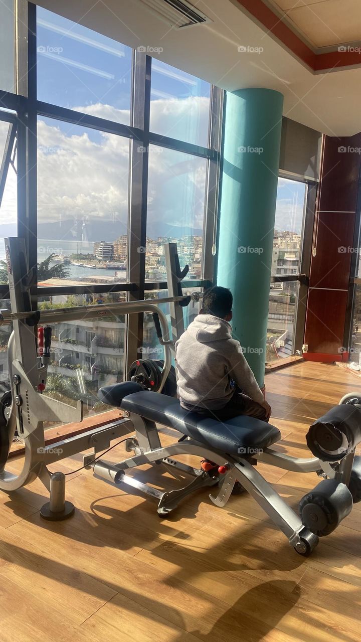 Young boy in a gym high above the city staring off into the distance.