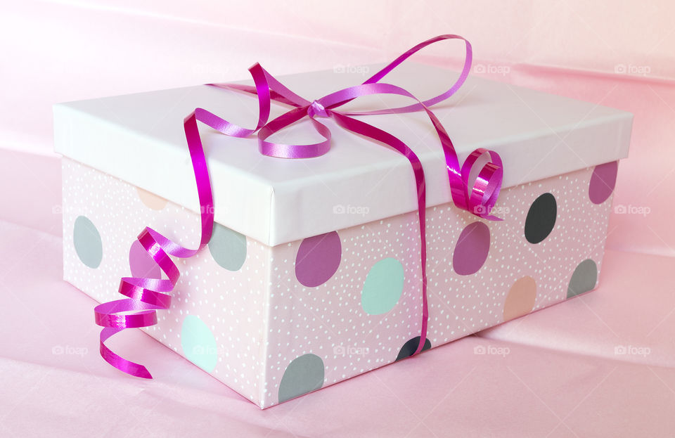 A rectangular pink spotted gift box tied with bright pink ribbon on a background of pink tissue paper.