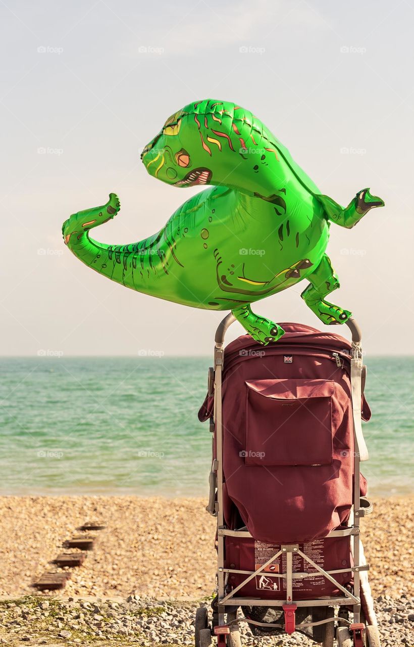 Dinosaur shaped helium balloon attached to a pushchair, looking out over a beach to the sea