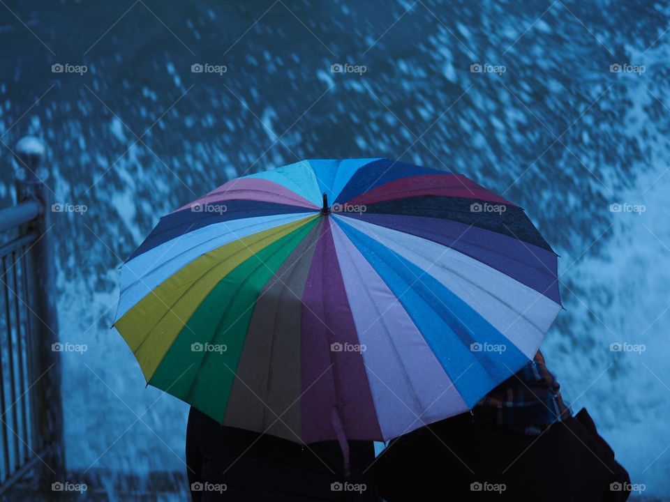 Two people with colourful umbrella sitting near sea in storm weather