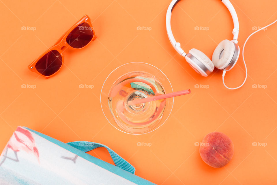 Sunglasses, glass with drink, headphones, peach, blanket on orange background. Minimal summer style