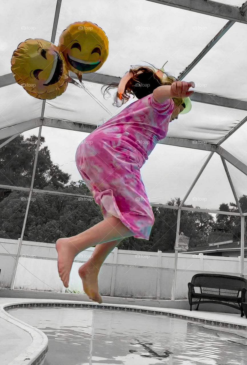 Smiley Faces Helium Balloons Seem To Pull The Girl Up In The Air While She Jumps In The Water With It In The Pool.