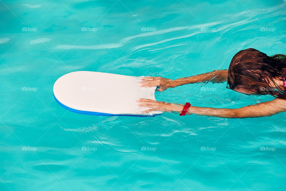 Woman learning to swim, practicing in swimming pool using a board. Candid people, real moments, authentic situations