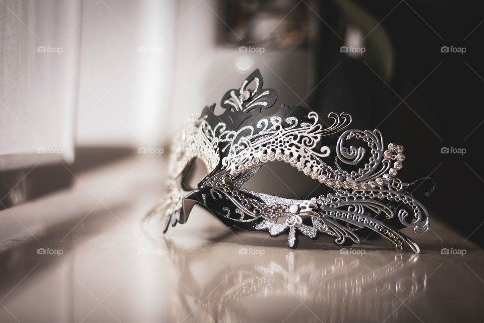 A portrait of a mysterious venetian mask on a window sill ready to be put on to go to a masked ball, carnaval or halloween party.