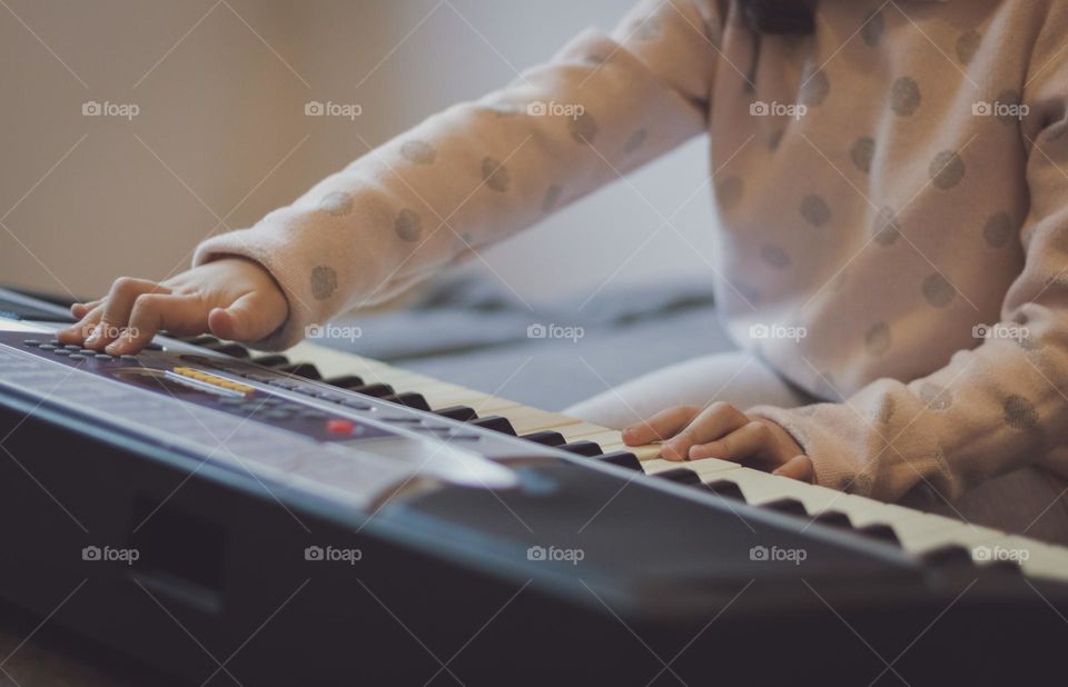 Hands of a little caucasian girl pressing her fingers on the keys of an electric piano while sitting on a sofa in the living room, side view close-up with depth of field. Music education concept, musical instruments.