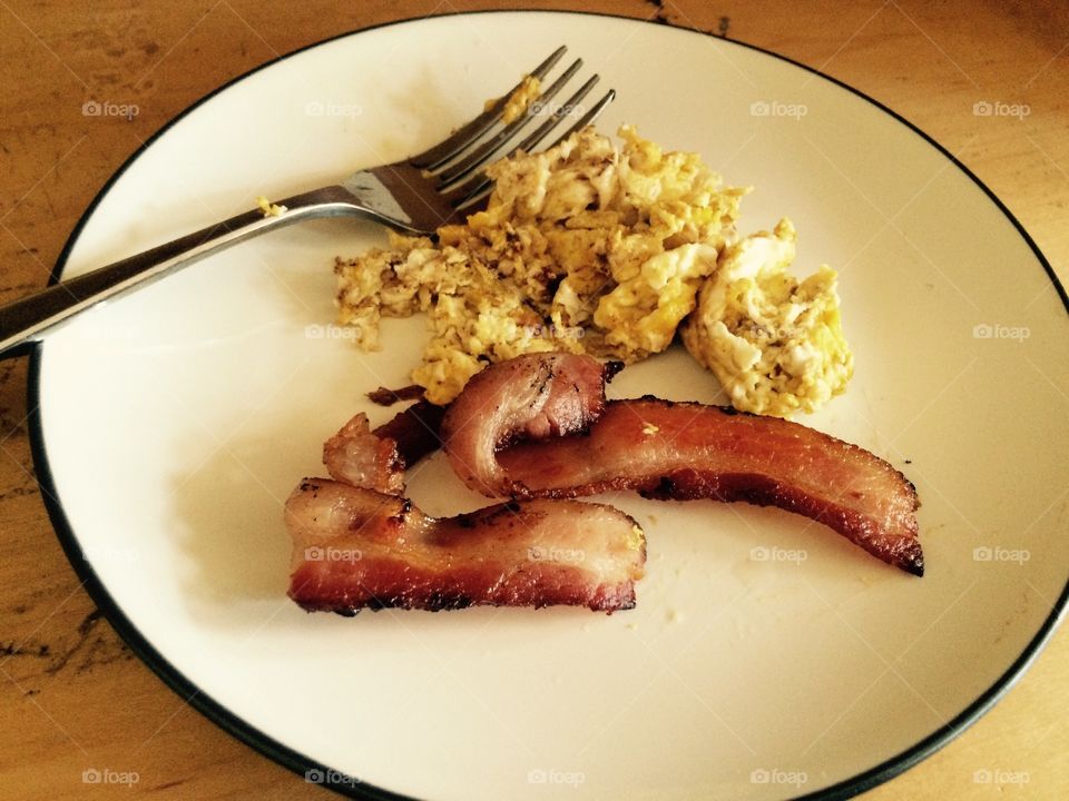 Bacon and eggs breakfast. A white plate with a fork and scrambled eggs and fried bacon