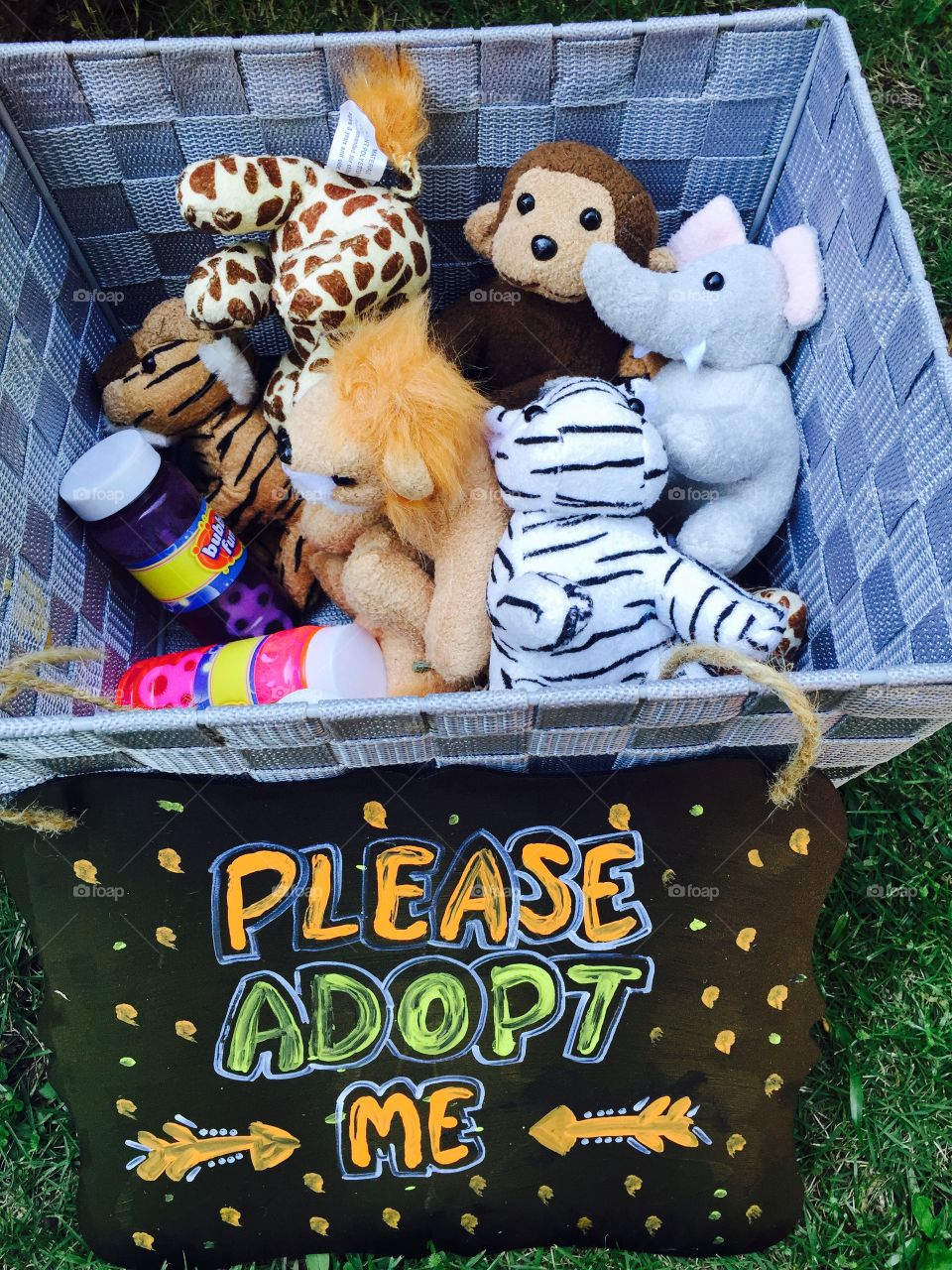 A basket full of  cute stuffed animals and a sign "saying please adopt me" on it . 
