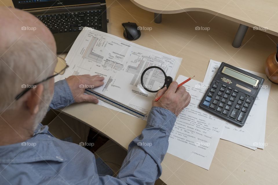the architect works with project documentation at the computer, in his right hand a pencil and a loupe