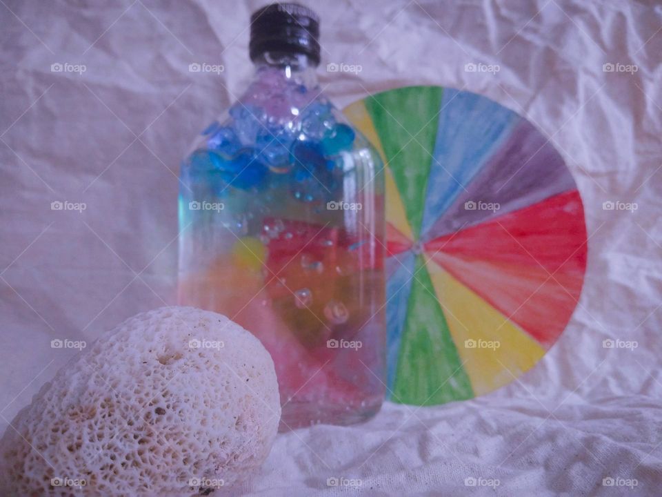 This is a colouful moment. There is a bottle with a full of colourful marbles.and also there is a colour plate behind the marble bottle. There is a sea shell too. this is very creative idea..