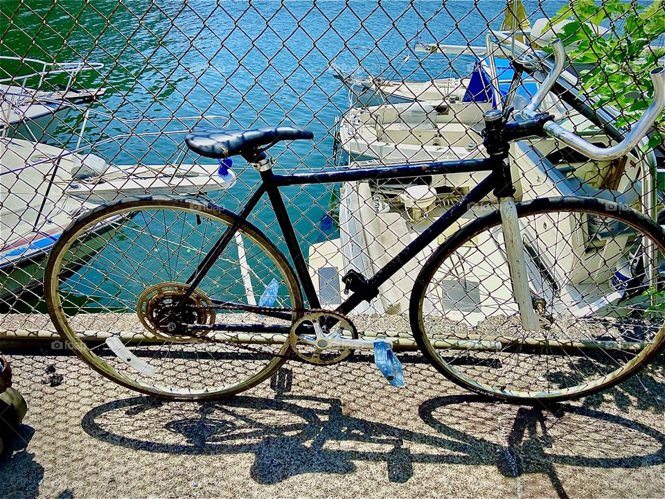 S bicycle stored by the building that the wall and wooden planks we use to walk to our boat, the „Salvation“ are leaning against. 2022. Hypnotic Productions