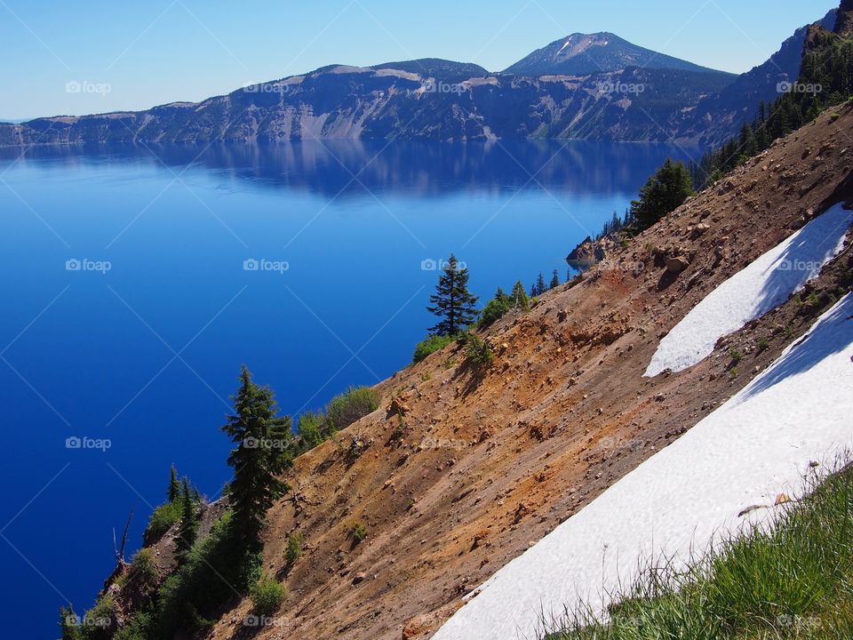 The jagged rim reflecting into the rich blue waters of Crater Lake in Southern Oregon on a beautiful summer morning with perfect clear blue skies. 