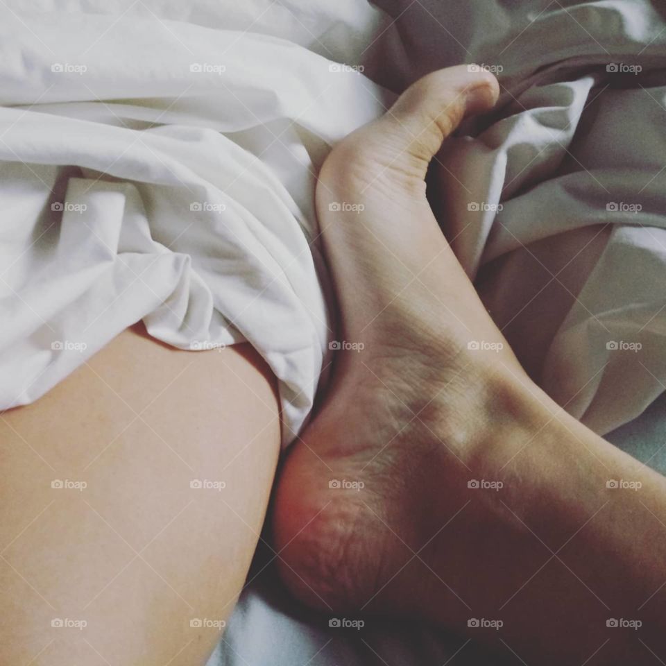 absract photo of womans feet and leg in bed between the sheets