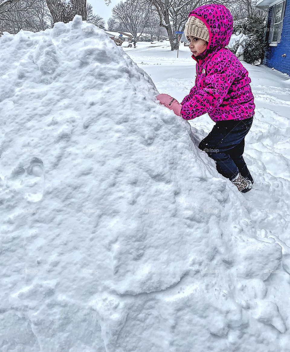Little girl climbs large mountain of snow, enjoying the magic of winter, seasons of the Midwest, winter is the best season 