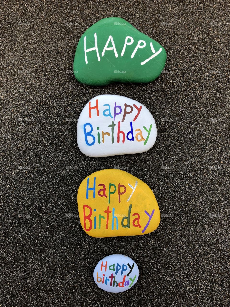 Many Happy Birthday stones over natural black volcanic sand 