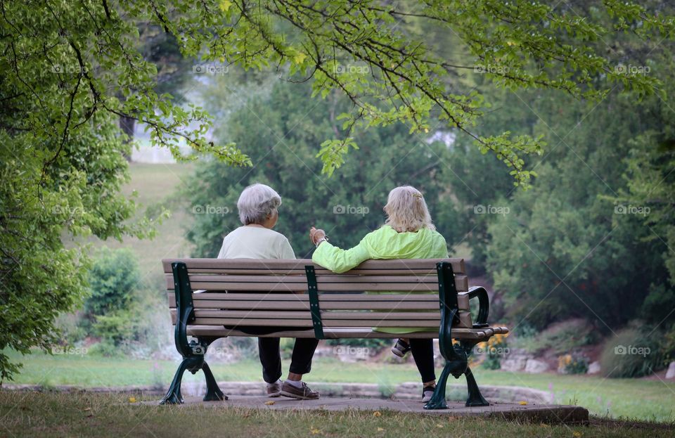 Two elderly ladies sit on a bench in the park