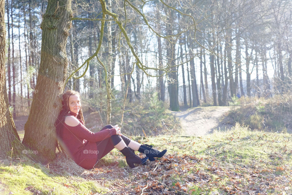 Beautiful young woman in the woods sitting against a tree